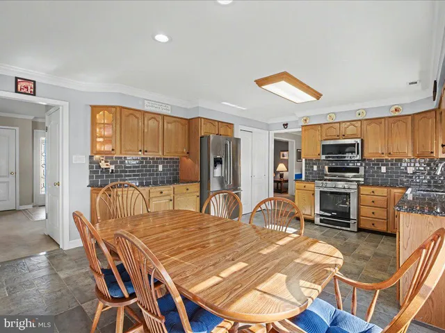 a kitchen with stainless steel appliances kitchen island granite countertop a table chairs and a refrigerator