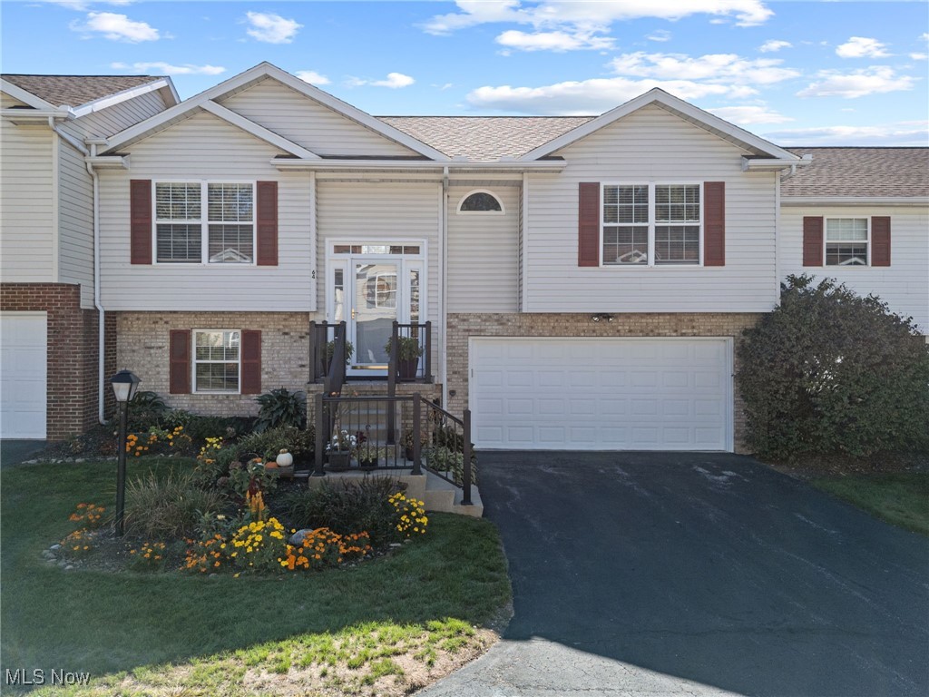 Split foyer home featuring brick siding, driveway, an attached garage, and roof with shingles