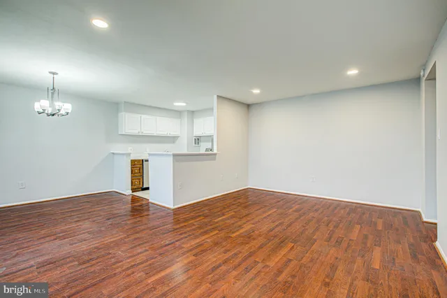 an empty room with wooden floor kitchen appliances and windows