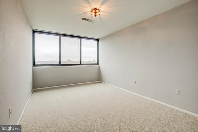 an empty room with chandelier fan and windows
