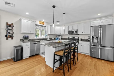 a kitchen with stainless steel appliances granite countertop a sink a stove a refrigerator and island with wooden floor
