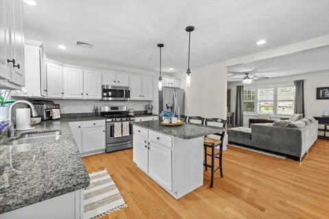 a kitchen with stainless steel appliances granite countertop a stove top oven a sink dishwasher a dining table and chairs with wooden floor