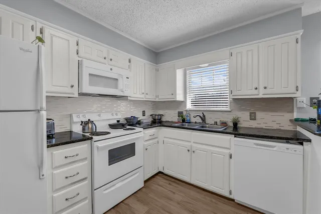 a kitchen with granite countertop white cabinets white appliances and a sink