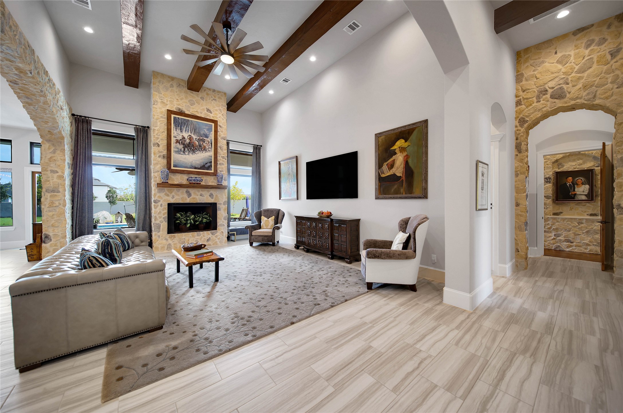 24718 Shadow Pond Spring, TX 77389 - Photo 8 of 49 Elegant living room featuring a stunning stone fireplace, high ceilings with wooden beams, and abundant natural light from large windows, creating a warm and inviting atmosphere.