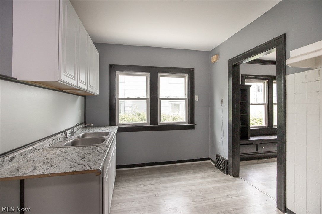 1868-1870 Lampson Road Cleveland, OH 44112 - Photo 27 of 36 Kitchen area featuring wood-finish flooring, white upper and lower cabinetry, a double stainless steel sink, and light-toned countertops