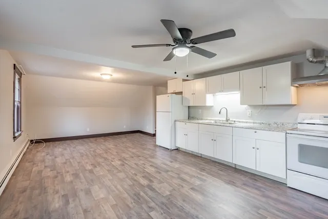 a kitchen with granite countertop a stove a sink and white cabinets with wooden floor
