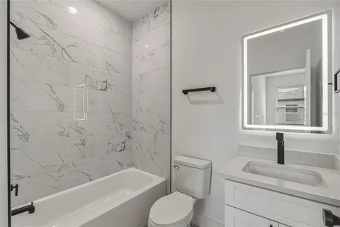 a bathroom with a granite countertop bathtub sink vanity mirror and toilet