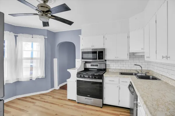 a kitchen with stainless steel appliances granite countertop a sink a stove a microwave a refrigerator a white cabinets and wooden floor