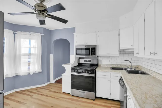 a kitchen with stainless steel appliances granite countertop a sink a stove a microwave a refrigerator a white cabinets and wooden floor