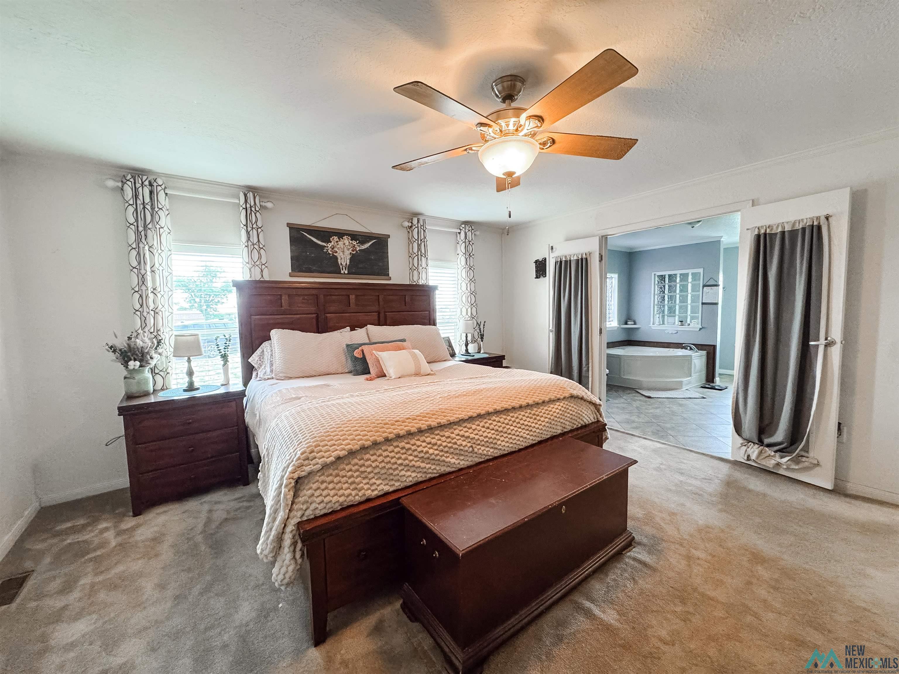 309 Crossbow Road Artesia, NM 88210 - Photo 15 of 31 Carpeted sleeping area with a ceiling fan, dual windows, and an en-suite bathroom featuring a jetted tub