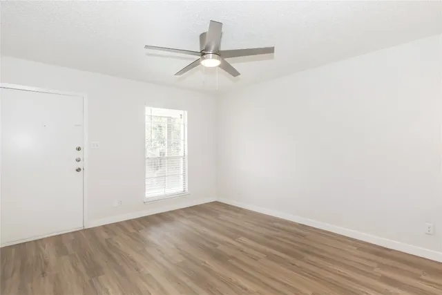 an empty room with wooden floor window and ceiling fan