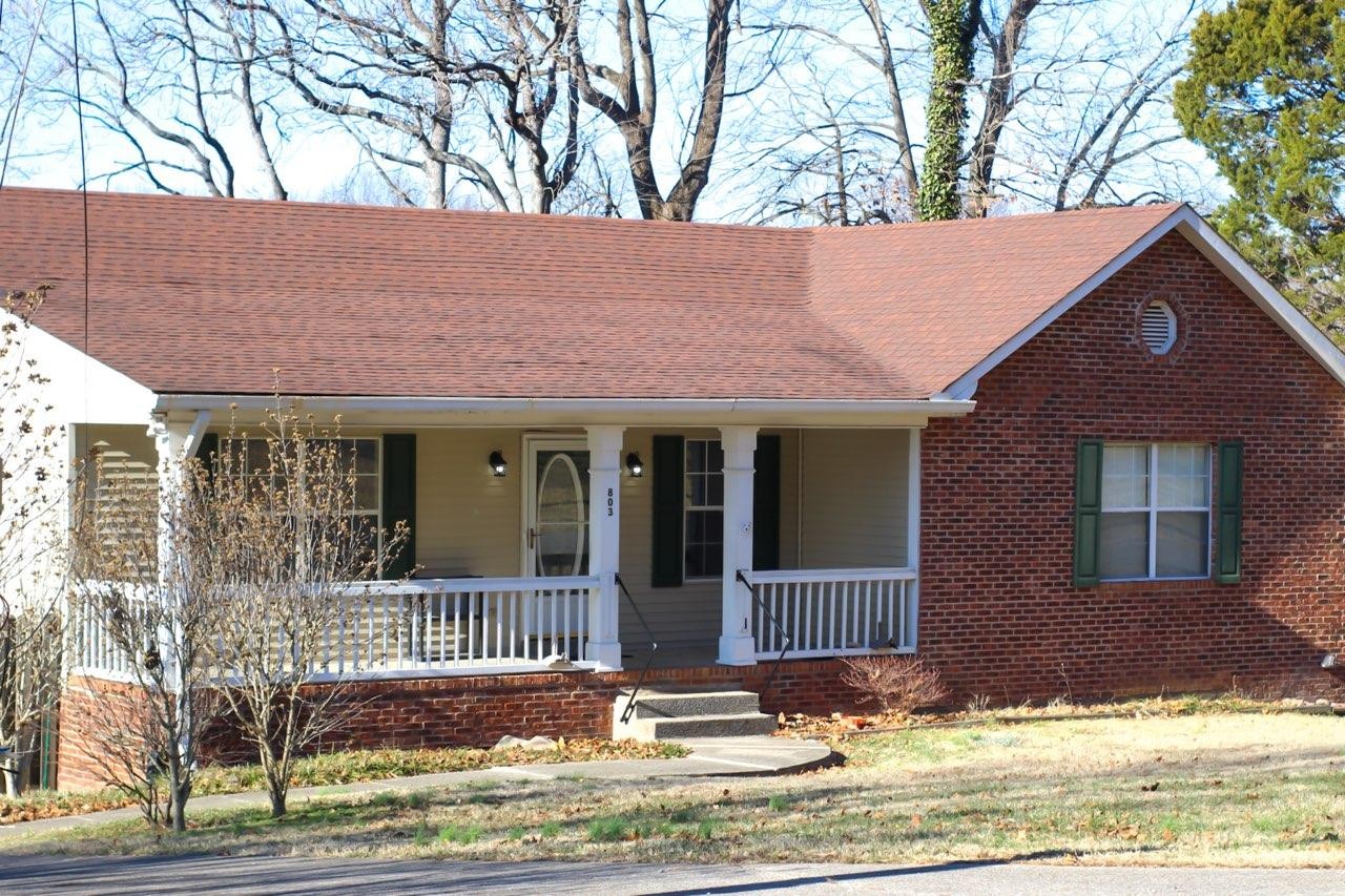 a view of a brick house with a large tree and wooden fence