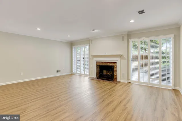 an empty room with wooden floor fireplace and windows