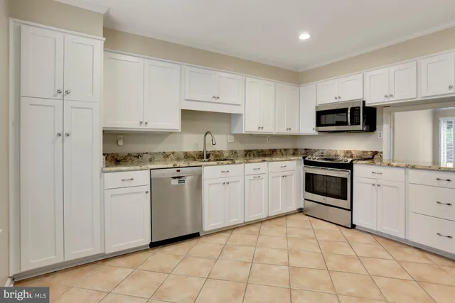 a white kitchen with granite top and stainless steel appliances