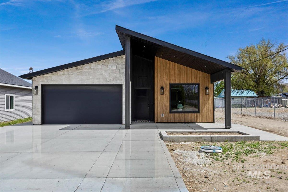 Contemporary exterior featuring a stone facade, wood-finish siding, a dark garage door, and a covered entry