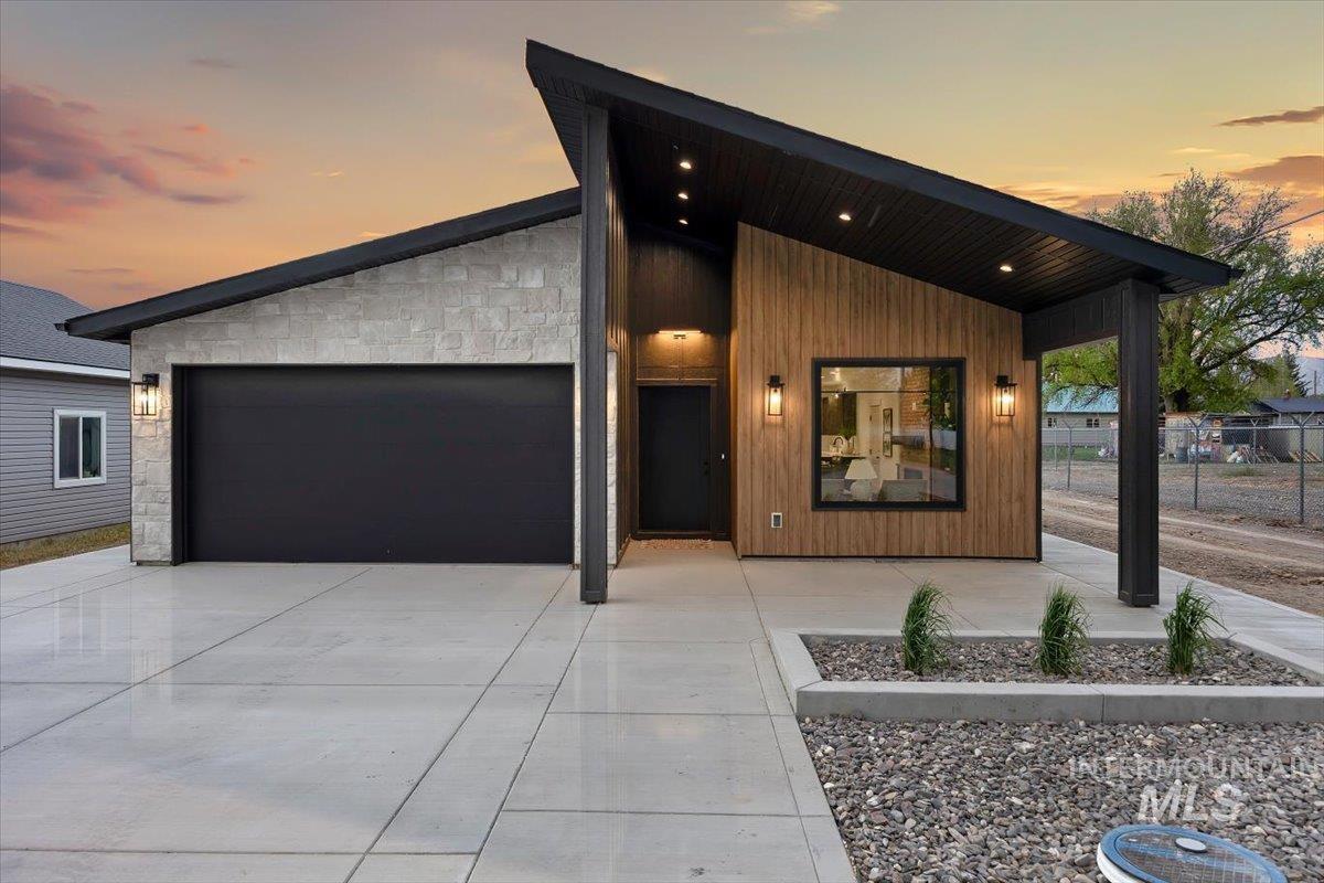Modern exterior featuring a prominent angled roofline, stone facade accents, wood-finish siding, a large black garage door, and recessed soffit lighting