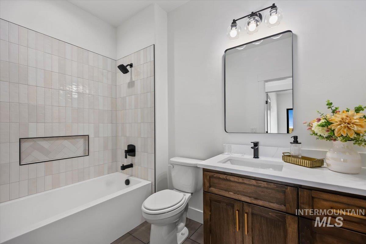 107 3rd Street West Declo, ID 83323 - Photo 22 of 25 Bathroom featuring a white tub, vertical subway tile shower surround with a herringbone accent niche, dark wood vanity with a white countertop and integrated sink, and matte black fixtures