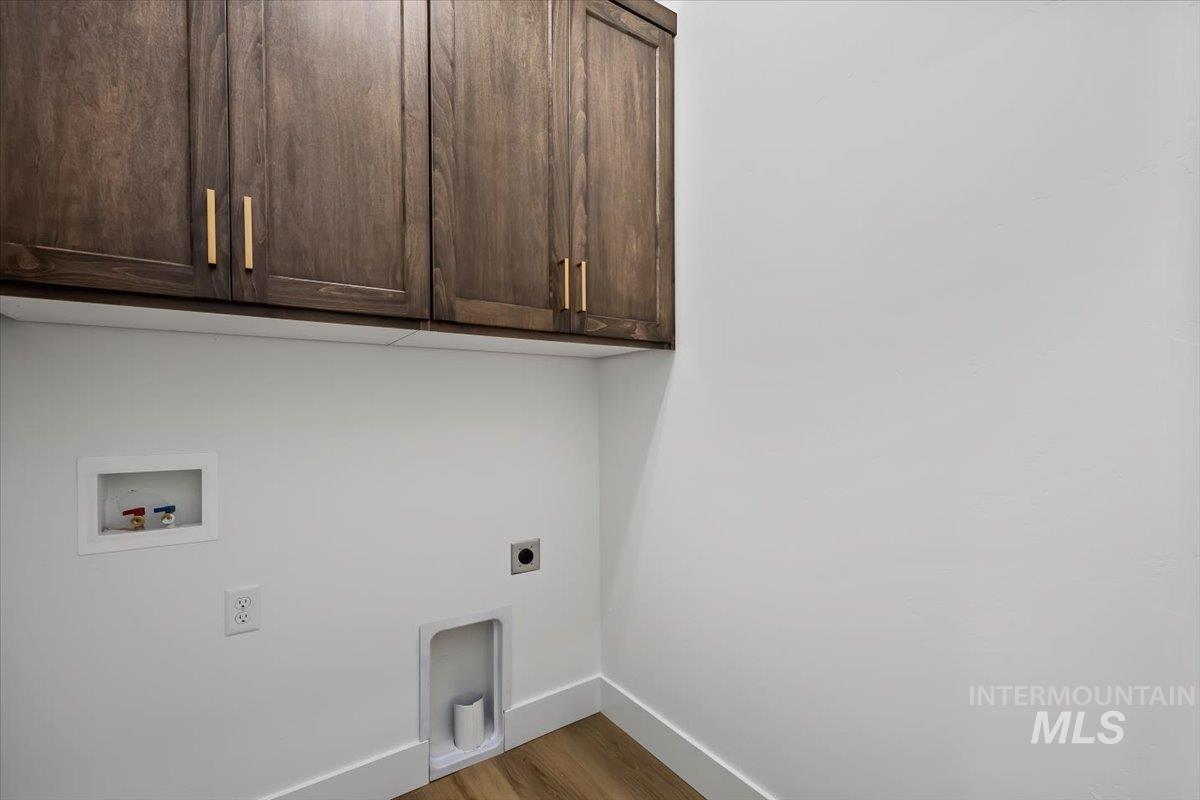 107 3rd Street West Declo, ID 83323 - Photo 23 of 25 Laundry area featuring dark wood-finish cabinetry with golden hardware, white walls, and wood-finish flooring