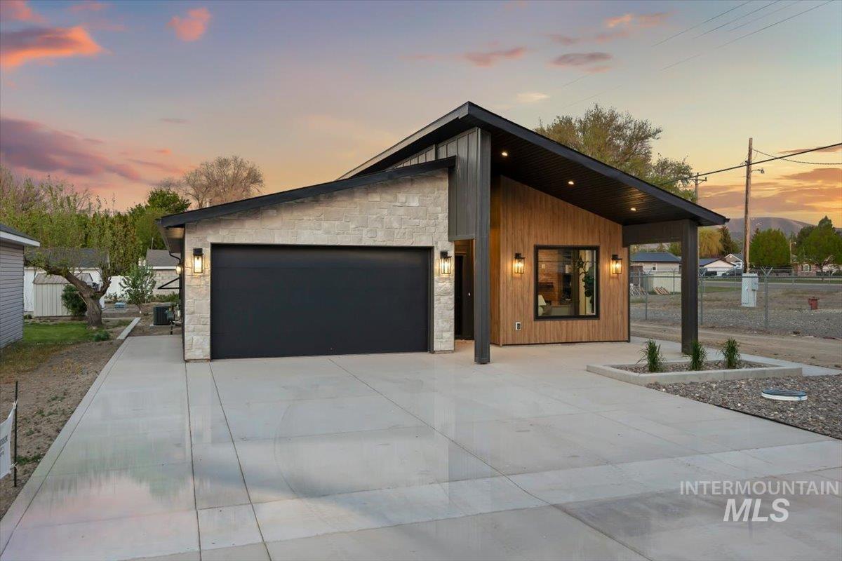 107 3rd Street West Declo, ID 83323 - Photo 25 of 29 Contemporary exterior with stone veneer and wood-finish siding, featuring a black garage door and a covered entry