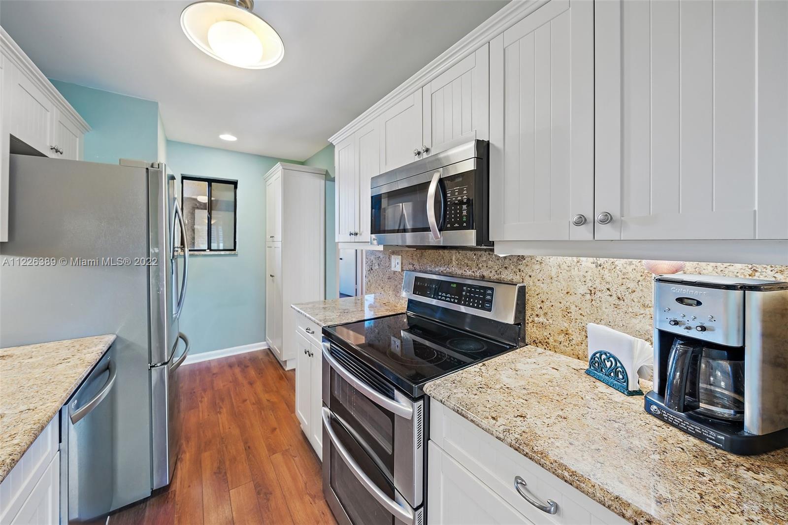 5335 Southeast Miles Grant Road, Unit 107 Stuart, FL 34997 - Photo 10 of 44 a kitchen with stainless steel appliances granite countertop a stove top oven a sink dishwasher and a microwave with wooden floor