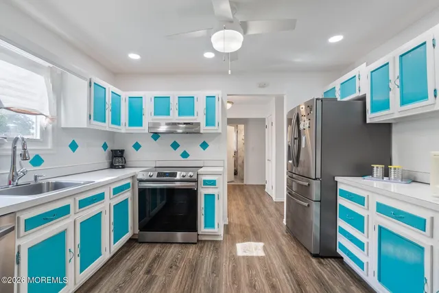 a kitchen with stainless steel appliances a stove a sink dishwasher a refrigerator white cabinets and wooden floor