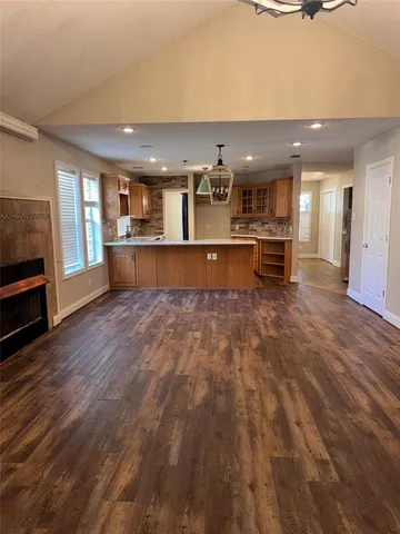 a living room with stainless steel appliances kitchen island granite countertop a refrigerator a stove a oven and white cabinets with wooden floor
