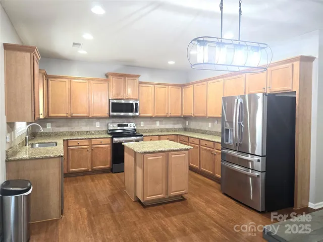 a kitchen with stainless steel appliances granite countertop a refrigerator a sink dishwasher a stove and white cabinets with wooden floor