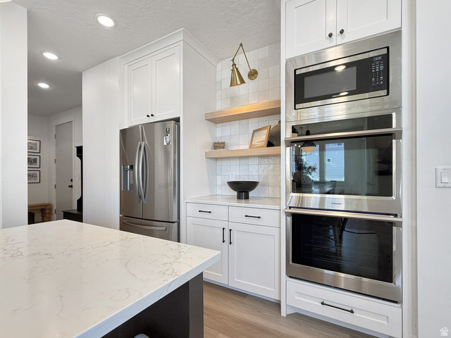 916 Rocky Mountain Way Elk Ridge, UT 84651 - Photo 13 of 54 Kitchen with stainless steel appliances, white cabinets, backsplash, open shelves, and light wood-style floors