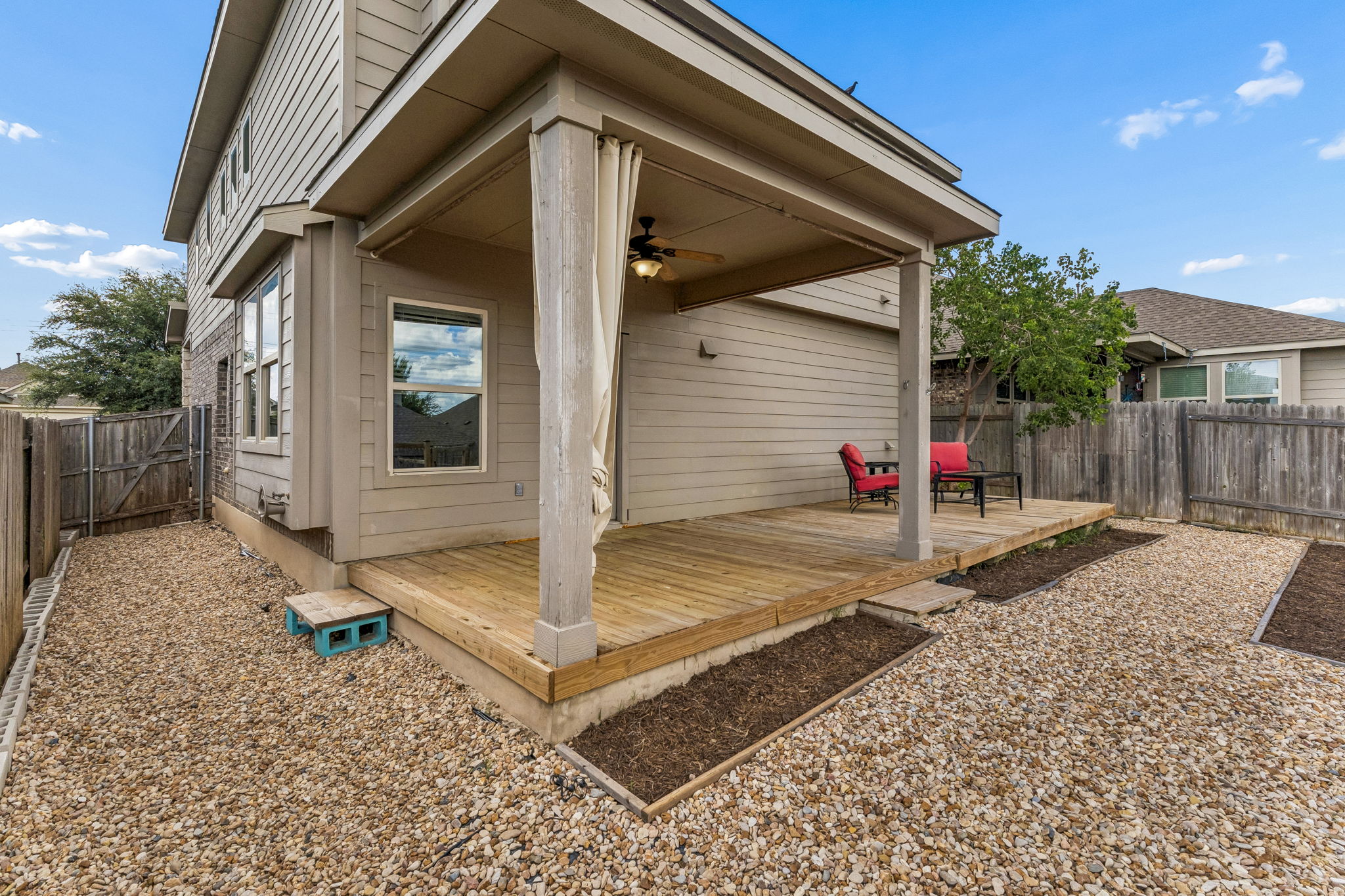 689 Nautical Loop Kyle, TX 78640 - Photo 31 of 34 A secluded outdoor deck with a ceiling fan offers a peaceful escape, overlooking a low-maintenance gravel yard with dedicated planting areas.