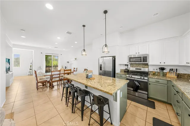 a open kitchen with stainless steel appliances granite countertop a stove top oven a sink a dining table and chairs with the wooden floor