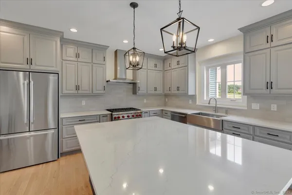 a kitchen with stainless steel appliances granite countertop a refrigerator a sink dishwasher a stove and white cabinets with wooden floor