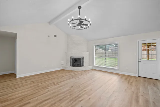 an empty room with wooden floor chandelier and windows