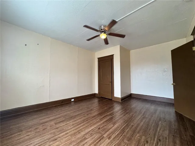 a view of an empty room with wooden floor and a ceiling fan