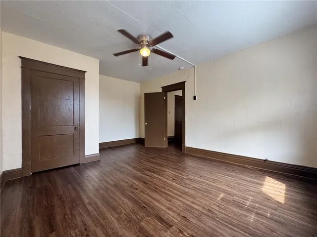 a view of an empty room with wooden floor and a ceiling fan