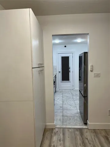 a view of a hallway with wooden floor and a refrigerator in a kitchen