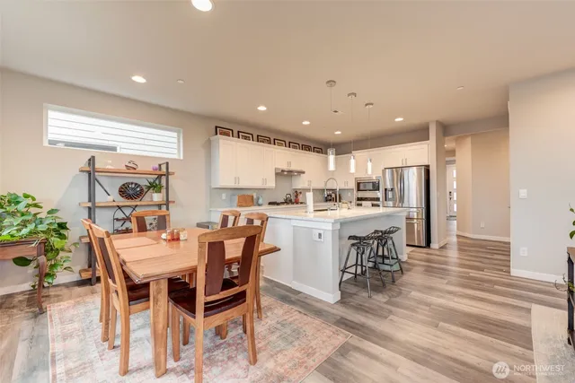 a dining hall with stainless steel appliances kitchen island granite countertop a dining table chairs and a refrigerator