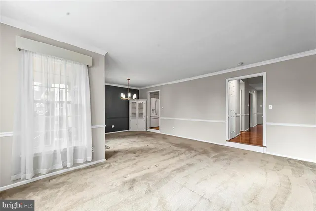 a view of an empty room with window and kitchen view