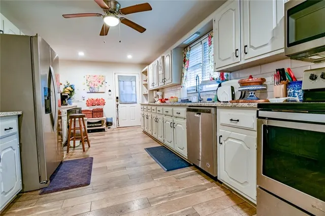 a large kitchen with stainless steel appliances kitchen island granite countertop a refrigerator a stove a sink dishwasher and white cabinets with wooden floor
