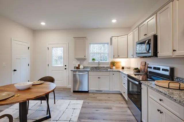 a kitchen with stainless steel appliances granite countertop a stove top oven a sink dishwasher and white cabinets with wooden floor