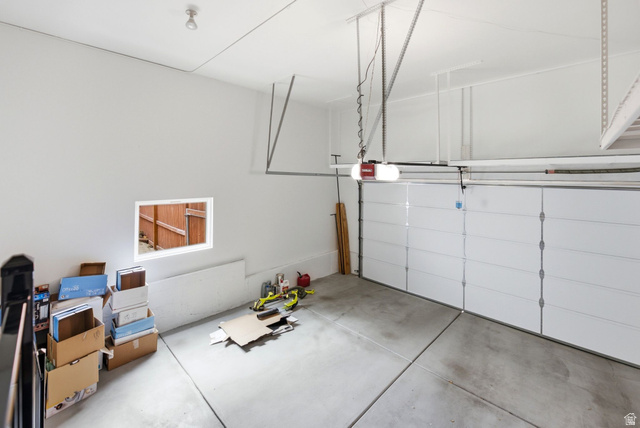 11875 South Elm Ridge Road Sandy, UT 84094 - Photo 33 of 53 Spacious garage featuring a concrete floor, white insulated garage door, automatic garage door opener, overhead lighting, and a small window for natural light