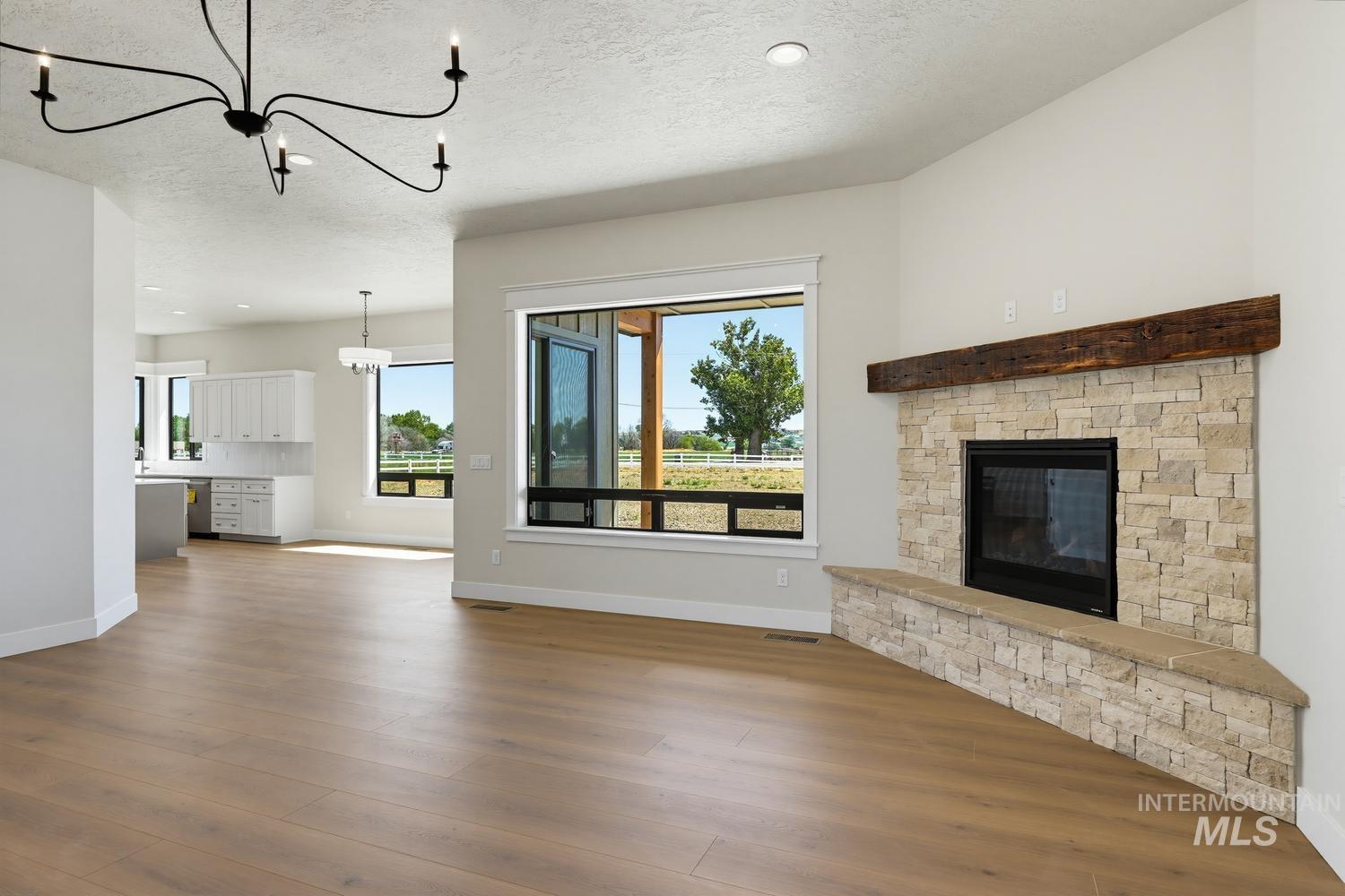 5054 Heritage Drive Marsing, ID 83639 - Photo 12 of 38 Spacious living area featuring a stone-clad fireplace with a wood mantel, large windows, and light wood-finish flooring