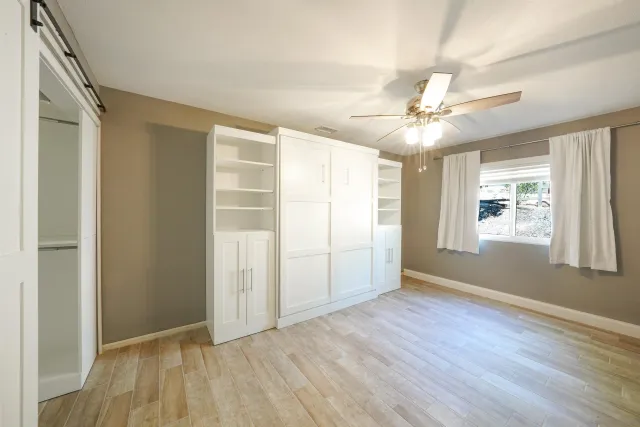 an empty room with wooden floor chandelier fan and windows