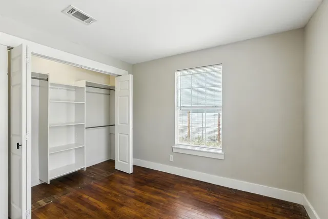 an empty room with wooden floor closet and windows