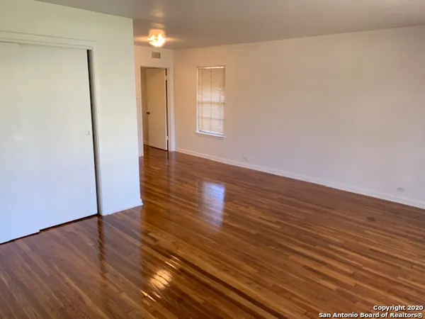 a view of an empty room with wooden floor and a window