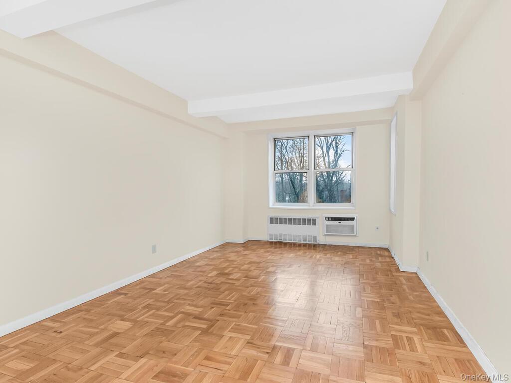 679 West 239th Street, Unit 1C Bronx, NY 10463 - Photo 4 of 13 Spare room with radiator heating unit, baseboards, an AC wall unit, and beamed ceiling