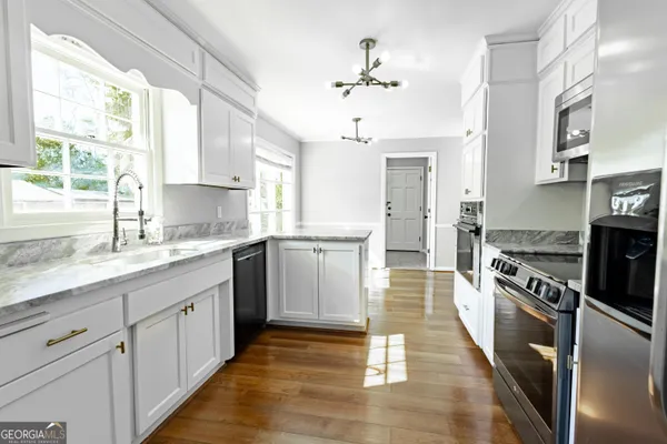 a kitchen with stainless steel appliances kitchen island granite countertop a stove a sink and white cabinets with wooden floor