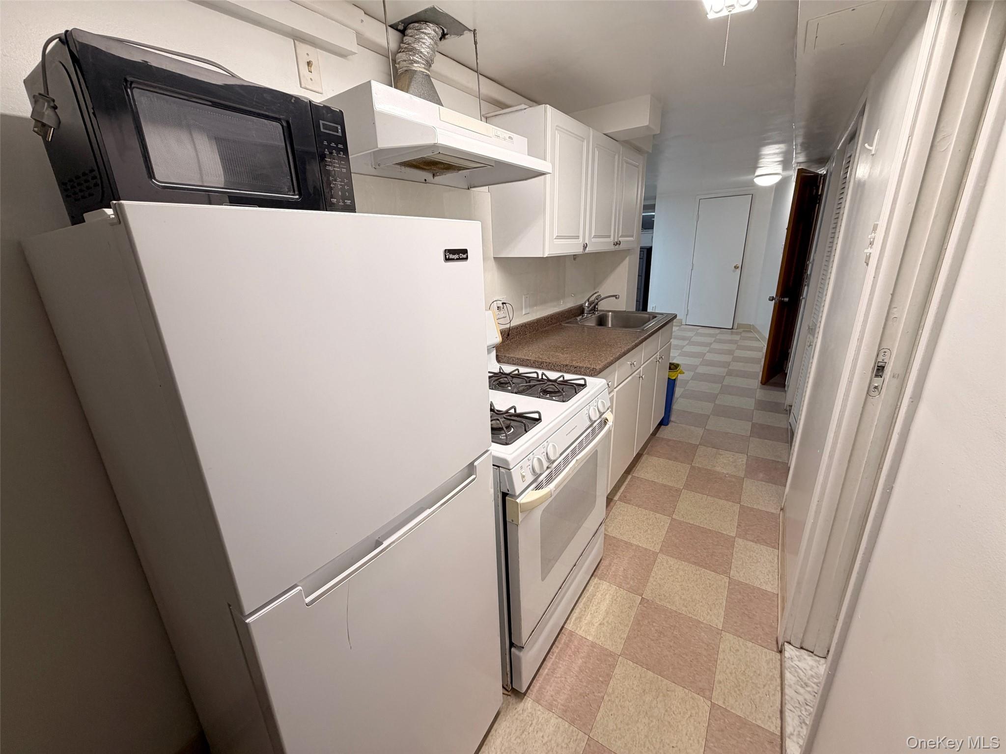 153-20 77th Road, Unit 1 Queens, NY 11367 - Photo 3 of 11 Kitchen with light flooring, white appliances, white cabinetry, exhaust hood, and dark countertops