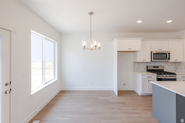 5228 South Acacia Drive, Unit 808 Mapleton, UT 84664 - Photo 9 of 22 Open-concept living space featuring wood-finish flooring, a contemporary chandelier, white shaker-style cabinetry, stainless steel appliances, and a tiled backsplash