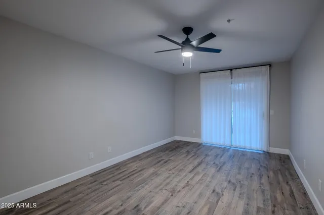 an empty room with wooden floor fan and windows