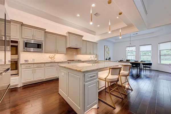 a kitchen with stainless steel appliances granite countertop a stove top oven a refrigerator a sink and white cabinets with wooden floor